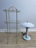 Full view of the small stand and the Space Age lamp side by side on floor against neutral wall.