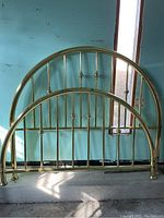Vintage brass bed headboard and footboard with curved tops leaning against wall, sunlight casting shadows.