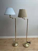Full view of two vintage brass swivel floor lamps showing both blue and beige shades, bases, and adjustable arms.
