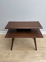 Front view of vintage mid century wooden table showing upper and lower shelf and tapered legs.