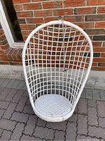 Front view of vintage white wicker hanging chair showing oval-shaped lattice back and woven seat with chain and hook attached at top.