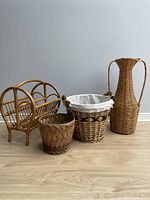 Photo showing four wicker/rattan items: magazine rack, tall vase, large lined basket, and smaller woven basket.