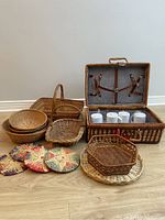 Full lot overview showing wicker picnic basket with interior cups, multiple wicker bowls, baskets, and woven trivets on floor.