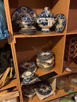 Overview of three shelves holding flow blue china pieces including tureen, plates and bowls