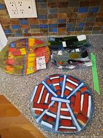 Photo showing colorful round cake plate with matching serving utensil, and multiple art glass plates arranged on countertop