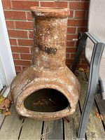 Front view of terra cotta chiminea showing its cylindrical chimney, large front opening and weathered surface.