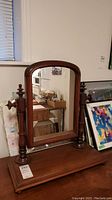 Front view of wood framed dresser mirror with arched top and turned wooden supports on rectangular base.