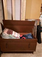 Front view of wooden storage bench with lid open showing various fabrics inside