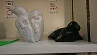 Two soap stone carved figurines placed side by side on a shelf, showing full view and relative scale.