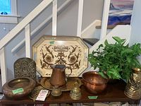 Overview photo showing two copper water pitchers, several brass bowls, bookends, decorative brass pots, flower pot with plants, and serving plater in the background.