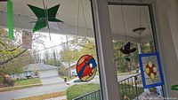 Four stained glass decorations hanging on window, showing various designs and colors including star, bird, butterfly, and floral panel