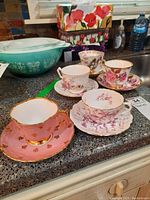 Five teacups with matching saucers arranged on a countertop showing variety of patterns and colors