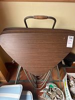 Three stacked vintage TV tables with triangular wooden tops and tubular metal legs in a metal rack with a handle.