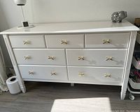 Full front view of white dresser showing three small upper drawers over four larger lower drawers with gold bow knobs