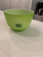 Side view of a smooth apple green blown glass bowl with a rounded shape and thick glass base.