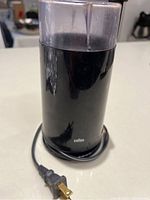 Front view of black Braun electric coffee grinder with power cord and transparent container.