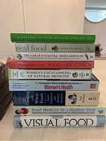 Nine books stacked showing titles and authors, focusing on food, nutrition, health, and natural medicine.