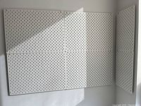 Three large and one small white IKEA pegboard panels mounted on two walls featuring vertical slots for hooks and accessories.