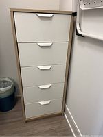Front view of slim vertical storage unit with 5 white drawers and faux wood frame