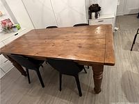 Angled view of full table top showing planked pine surface and turned legs, chairs partially visible.