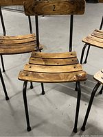 Front angle of chair number 2 showing curved slatted wood seat and black steel frame with rubber feet