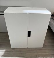 Front view of the closed white cabinet showing the two doors and central cut-out handles.