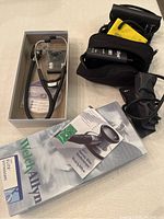 Welch Allyn Harvey Elite stethoscope in original box with instruction manual and replacement parts, alongside blood pressure cuffs and sphygmomanometer in carrying cases.