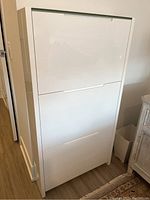 Front view of the closed white high gloss shoe cabinet showing the sleek modern design with three horizontal pull-down compartments.