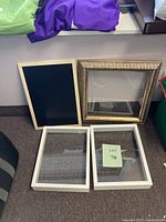 Five items including a gold-colored frame with glass, two white rectangular shadow boxes with glass, and one blackboard with white frame and hooks.