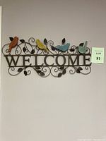 Full front view of the metal welcome sign with four colorful birds perched above the word 'WELCOME'.