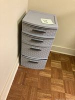 Front and angled view of the gray plastic 4 drawer weave patterned storage unit sitting on parquet floor