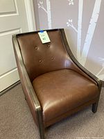 Full view of brown faux leather club chair showing front-facing seat, backrest with button tufting, and wooden arms and legs.