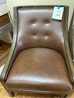 Front view of the brown faux leather club chair showing smooth upholstery and four button tufts on the inner backrest with wood arm frames.