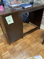 Front and left side view of brown pressed wood office desk, showing work surface and side panel with lot identification.