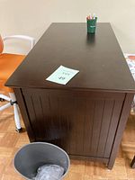 Full view of brown pressed wood office desk with wainscoting look on the side panel, dark finish, rectangular top with minor surface wear.