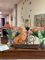 Overview of the cat outline lamp placed centrally on a wooden surface flanked by two jars with faux floral arrangements featuring orange flowers and greenery, plus a third jar with similar flowers.