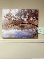 Front view of canvas print showing autumn tree branches over a calm lake reflecting sky and clouds.