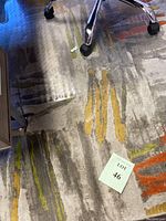 Photo showing the rug beneath an office chair with orange, yellow, and gray lines on a soft gray background, mild dirt visible.