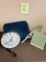 Lot arranged showing blue lumbar support pillow, round wall clock, one decorative blue bird, and mail organizer against a beige wall.