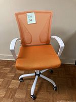 Full view of the orange mesh office chair with white armrests and base on casters, showing overall structure and design.
