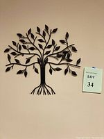 Full view of the black metal tree of life wall art mounted on a beige wall showing its shape and size relative to the wall.