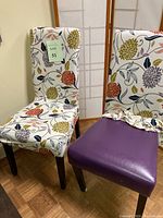Two standard size dining chairs, one showing the floral cover fully on the chair, the other beside it with the floral cover partially removed revealing the solid purple vinyl padded seat and wooden legs.