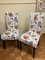 Two purple dining chairs with floral covers side by side on wooden floor.