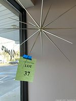 Silver spike hanging art piece attached near window, showing style and size.