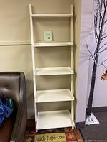 Full view of white 5-tier ladder shelf unit positioned adjacent to a brown couch and decorative rug.