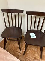 Two brown Windsor classroom chairs showing vertical spindle backs and curved seats.