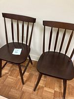 Pair of brown wooden Windsor classroom chairs shown side by side against white wall and parquet flooring.