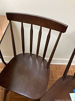 Close-up photo of the top portion of a brown wooden Windsor style classroom chair showing curved top rail and vertical spindles on the backrest.