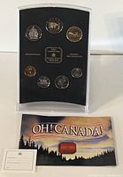 Front view of 7 Canadian coins displayed in black foam insert within clear plastic case, accompanied by certificate and decorative sleeve.