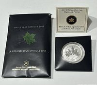 Photo of coin with original packaging and information card showing maple leaf design and year 2012.
